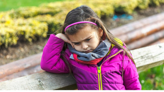 Young child sitting on a bench with head resting on hand, appearing emotionally overwhelmed and withdrawn during a back-to-school transition