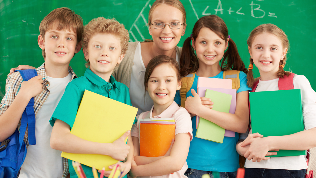 Smiling teacher with a group of happy primary school learners in front of a green chalkboard – building brighter futures for children with ADHD.